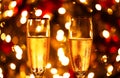 A closeup of two champagne glasses in front of a Christmas tree with blurry lights in the background. Royalty Free Stock Photo