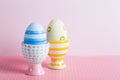 Closeup two colorful painted Easter eggs in vibrant modern egg stands on pastel pink background
