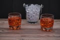Closeup of two glasses of whiskey with ice on a wooden table near an ice bucket