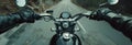 Closeup of two hands on motorcycle handlebars, motorcyclist on paved road