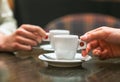 Two people holding cups of coffee sitting in cafeteria.