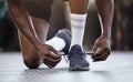 Closeup of unknown african american athlete kneeling and tying shoelaces before workout in gym. Strong, fit, active
