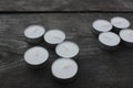 Closeup of unlit white tea candles on dark rough wooden table background outdoors. Top view, copy space