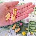 Closeup various colorful medicines in hand. In the background, one hudred European banknotes Ã¢â¬â Euro.