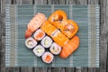 Closeup of various kinds of sushi rolls with salmon, sashimi and other slices of raw fish served on a green bamboo mat on rustic Royalty Free Stock Photo