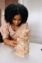 Closeup vertical portrait of serious African American woman playing tower block with diverse friends, taking out one