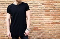 Closeup view of bearded muscular man wearing black tshirt and jeans posing outside. Empty brown grunge brick wall on the