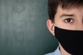 Closeup view of boy wearing mask near chalkboard, space for text. Child safety Royalty Free Stock Photo