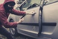 Closeup view of carjacker trying to open car with pick-lock. Masked man squats and breaks someone`s car looking to the