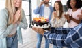 Closeup view of cheery multiracial people presenting birthday cake with lit candles to young blonde woman at home