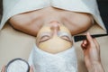 Closeup view of cosmetologist applying face mask on attractive woman in spa salon