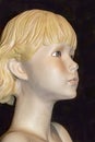 Closeup view of face of old retro mannequin girl with short blond hair and a chip in her nose and a spider behind her ear against