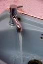 Closeup view of a gray color washbasin in which water is flowing through an open tap; pink wall Royalty Free Stock Photo