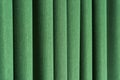 Closeup view of green curtain in thin and thick vertical folds made of dense fabric.Textured materials and textiles.