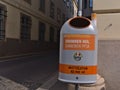 Closeup view of a grey and orange colored garbage can in the historic center of Vienna, Austria with funny slogan.