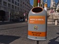 Closeup view of a grey and orange colored garbage can in the historic center of Vienna, Austria with funny slogan.