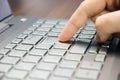 Closeup view of a hand with a finger press the Enter key on the silver keyboard laptop lying on a wooden mat Royalty Free Stock Photo