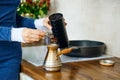 Closeup view of hand with spoon with ground coffee near a turk