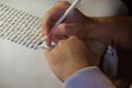 Closeup view of the hands of a Jewish scribe writing the Hebrew text of the Torah or Bible on parchment using a feather quill and