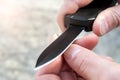 Closeup view of male hands sharpening a small thin wooden stick with a black pocket out the front knife with a sharp blade