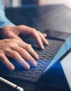 Closeup view of male hands typing on electronic tablet keyboard-dock station. Man working at office.Vertical,sunlight