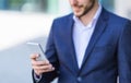 Closeup view of man in business suit using his smartphone in urban area