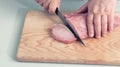 Closeup view man in the kitchen is cutting pork on cutting board