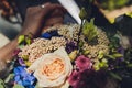 Closeup view of newlyweds hands holding colorful wedding bouquet. Bride and groom wearing wedding rings. Outdoor Royalty Free Stock Photo