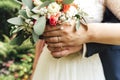 Closeup view of newlyweds hands holding colorful wedding bouquet. Bride and groom wearing wedding rings. Outdoor Royalty Free Stock Photo