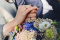 Closeup view of newlyweds hands holding colorful wedding bouquet. Bride and groom wearing wedding rings. Outdoor Royalty Free Stock Photo