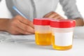 Closeup view of nurse writing urine analysis results at table, focus on container with sample Royalty Free Stock Photo