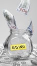 Closeup view of a pile of cash money with flying money entering a glass jar with note paper with saving text