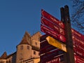 Closeup view of signpost pointing the directions of major destinations and landmarks with historic castle in background.