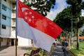 Closeup view of Singapore flag waving in the wind, cyclists riding by, on bright sunny day. HDB neighbourhood in background