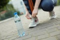 Closeup view of sportswoman lacing sneakers outdoors, focus on bottle with water Royalty Free Stock Photo