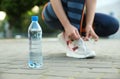 Closeup view of sportswoman lacing sneakers outdoors, focus on bottle with water Royalty Free Stock Photo