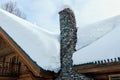 A closeup view of a stone chimney attached to a remote log cabin covered in freshly fallen snow.