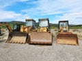 Closeup view of three backhoe loaders on a gravel road