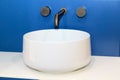 closeup view of white sink with modern simple faucet mounted in blue wall