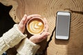 Closeup view woman hands holding cup of coffee. mobile smartphone at slab wooden table. space mockup for design layout. Sunlight. Royalty Free Stock Photo