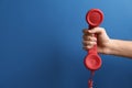 Closeup view of woman holding red corded telephone handset on blue background, space for text. Hotline concept Royalty Free Stock Photo