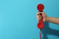 Closeup view of woman holding red corded telephone handset on light blue background  space for text. Hotline concept Royalty Free Stock Photo