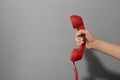 Closeup view of woman holding red corded telephone handset on light grey background, space for text. Hotline concept Royalty Free Stock Photo