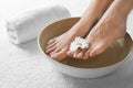 Closeup view of woman soaking her feet in dish with water and flower on white towel