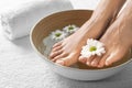 Closeup view of woman soaking her feet in dish with water and flowers on white towel.