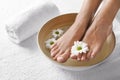 Closeup view of woman soaking her feet in dish with water and flowers on white towel. Spa treatment