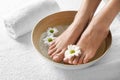 Closeup view of woman soaking her feet in dish with water and flowers on white towel, space for text.