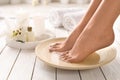 Closeup view of woman soaking her feet in dish with water on wooden floor. Spa treatment