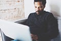 Closeup view of young African man using laptop while sitting sofa at his modern coworking studio.Concept full