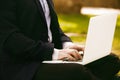 Closeup View of young businessman in formalwear typing on laptop keyboard while sitting at city green grass outdoor Royalty Free Stock Photo